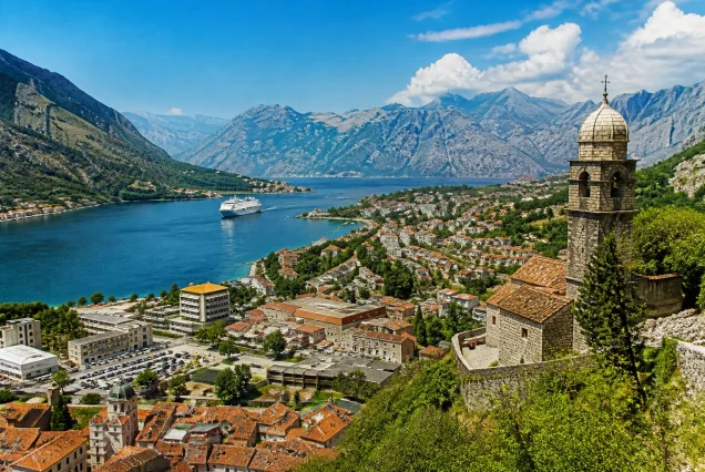Karadağ'ın Kotor kasabasının tarihi taş evleri, kırmızı kiremit çatılar ve etrafını saran yeşil dağlar ile derin mavi fiyort manzarası