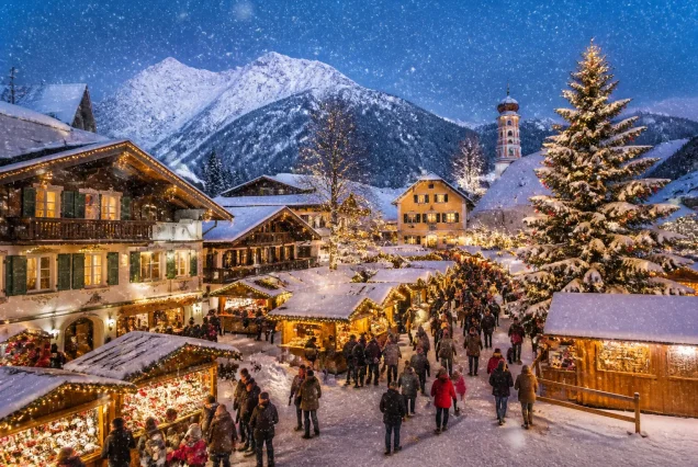 Kardan kaplı Alp Dağları önünde Bavyera Noel Pazarında renkli ışıklar ve süslemelerle dolu geleneksel pazar alanı