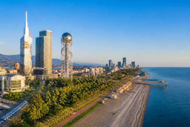 Karadeniz kıyısında Batum'un modern sahil şeridinin gün ışığındaki görüntüsü, içinde Alfabe Kulesi ve palmiye ağaçları.