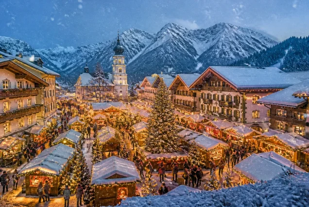 Kardan kaplı Alp Dağları önünde Bavyera Noel Pazarında renkli ışıklar ve süslemelerle dolu geleneksel pazar alanı