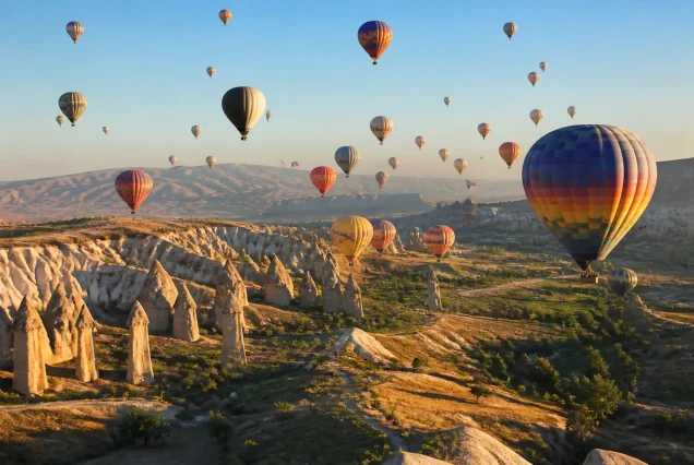 Kapadokya'da gün doğumunda peribacaları arasında uçan sıcak hava balonları ve doğal vadiler